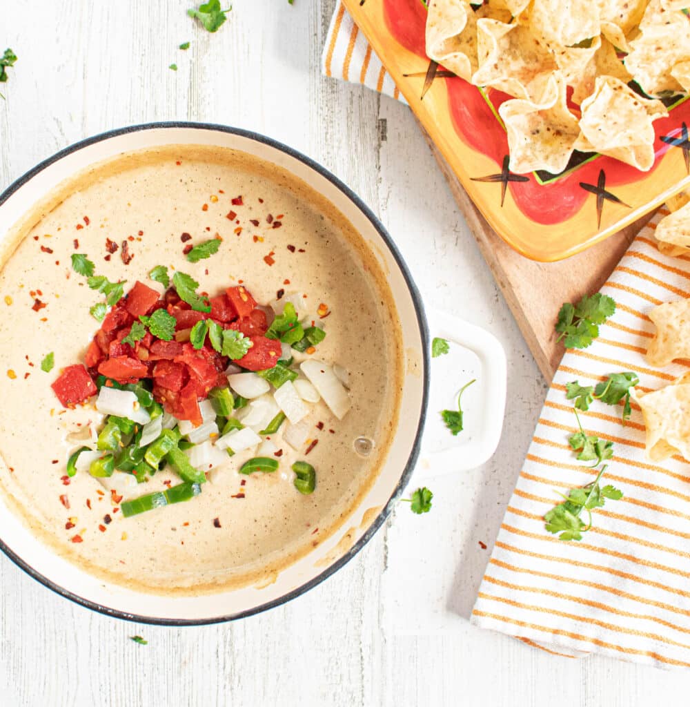 overhead of finished White Cauliflower Queso Dip Recipe in a white enameled cast iron Dutch oven with tortilla chips in a Mexican platter.