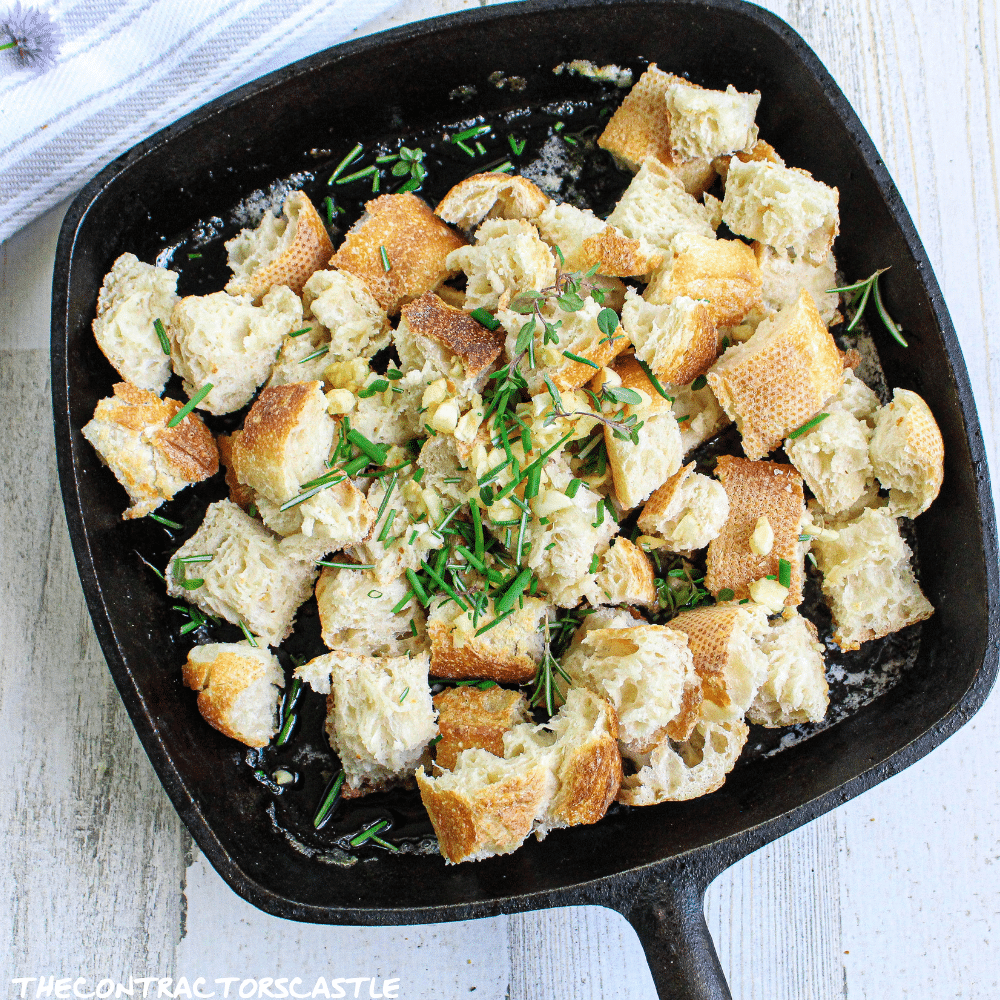 close up of unbaked croutons with fresh herbs in a cast iron skillet.