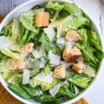 Caesar Salad with homemade croutons and shaved parmesan cheese in a white bowl on a mustard yellow towel