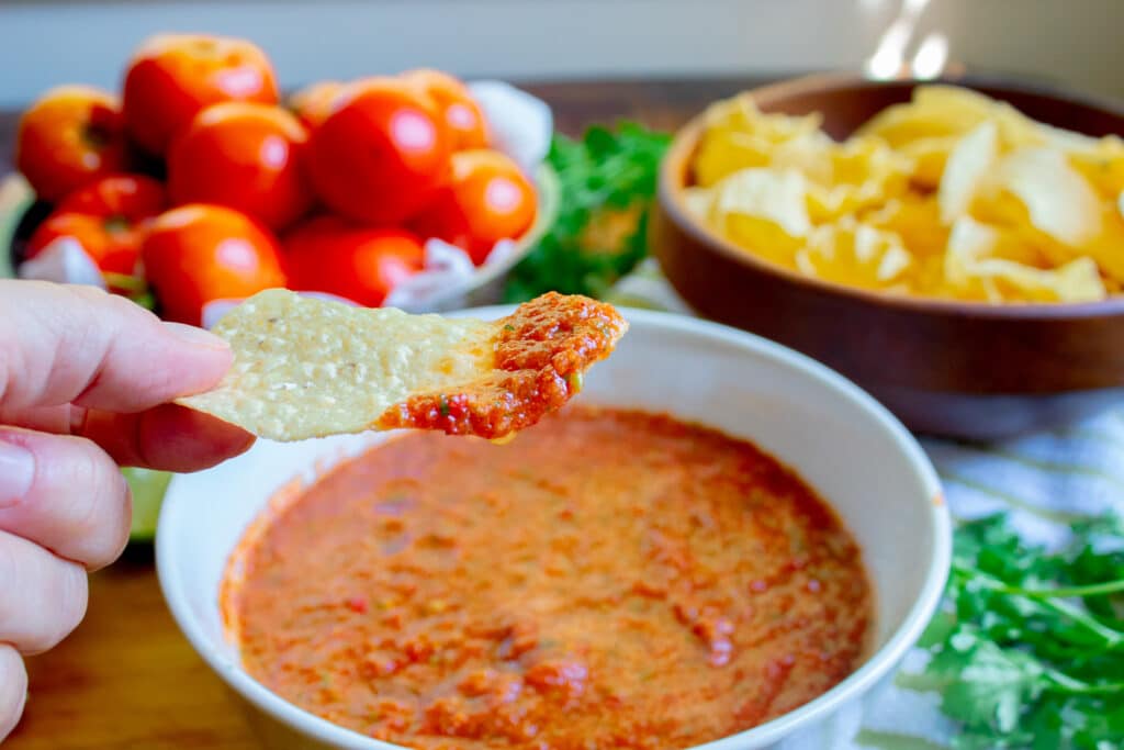 fresh garden salsa on a chip over a white bowl full of salsa