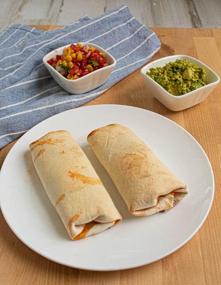 Air fryer Beef Burritos without toppings on a white plate with Tomato jalapeno relish and guacamole seperate in small white bowls