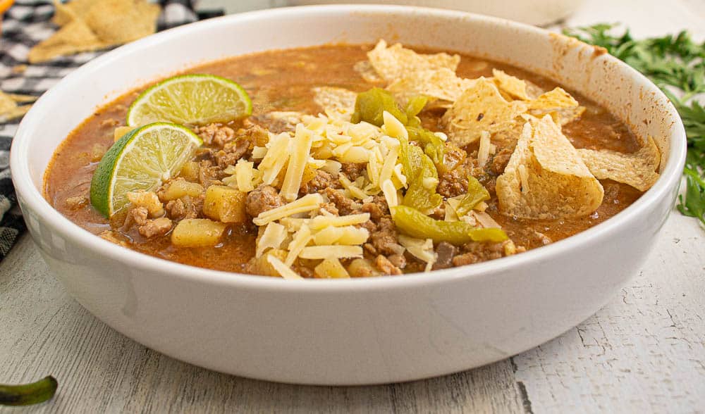 ground turkey green chili in a white bowl with tortilla chips, cheese, lime slices and big chunks of green chilis