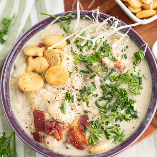 bowl of light clam chowder with oyster crackers bacon chives parsley in a purple bowl