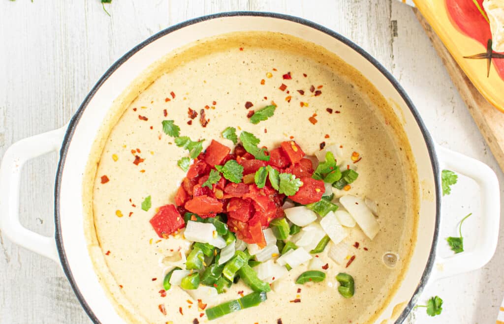 Light and creamy white cauliflower queso dip in a white dutch oven with peppers, onion, rotel tomatoes, and cilantro on top.