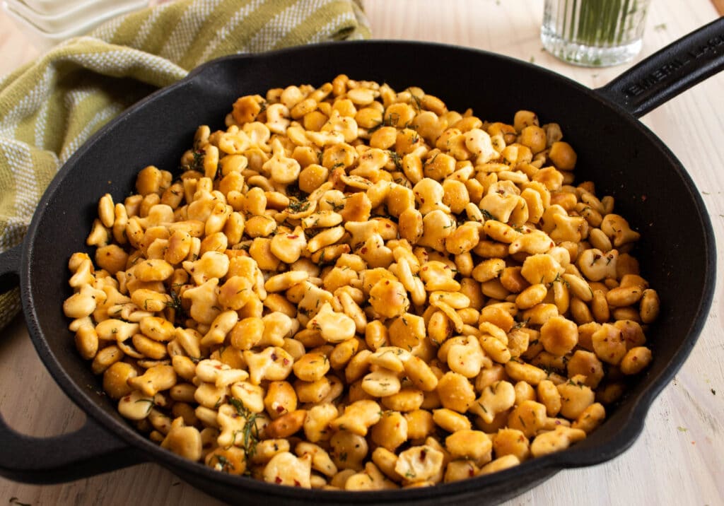 seasoned italian goldfish crackers in a large cast iron skillet on a white table with a green and white striped towel.