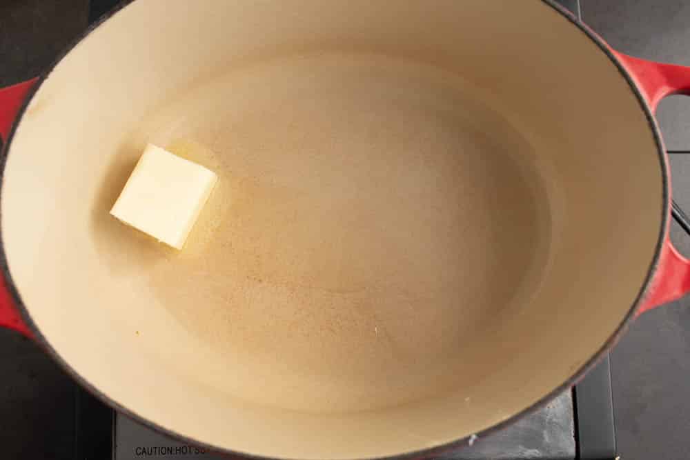 Red oval Dutch Oven with 2 tablespoons of butter starting to melt.