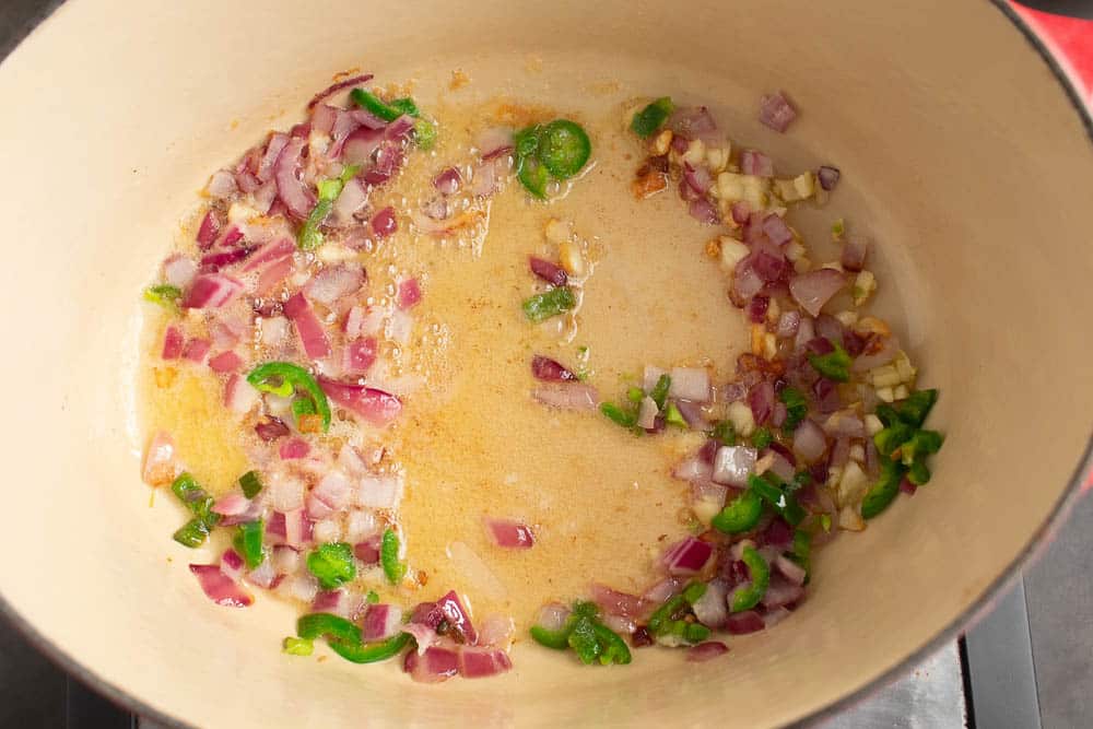 Onions, garlic, and jalapeno peppers sauting in butter in an oval dutch oven.