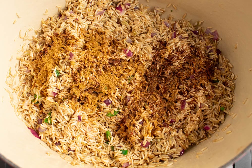 Rice and sauted vegetable butter mixture in a dutch oven with seasonings sprinkled in.