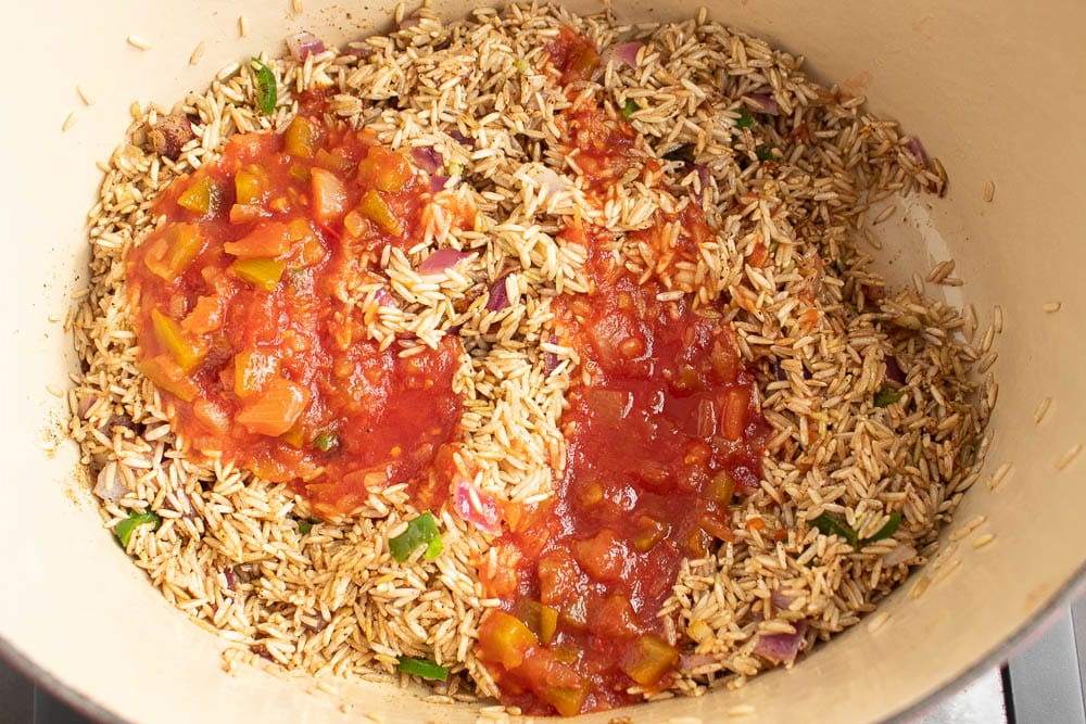 Rice and sauted vegetable butter mixture in a dutch oven with seasonings and salsa sauce on top.