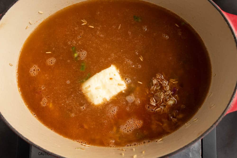 Rice and sauted vegetable butter mixture in a dutch oven with seasonings and salsa with broth and butter added in.