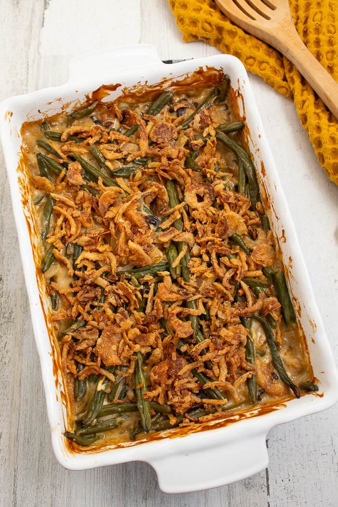 Cooked green bean casserole in a white rectangle casserole dish with unbaked canned french fried onions on top.