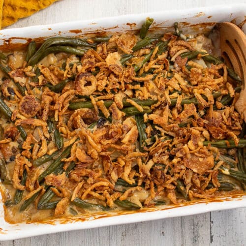 Cooked green bean casserole in a white rectangle casserole dish with unbaked canned french fried onions on top.