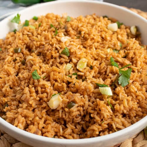 45 degree angle of a white bowl of mexican baked brown rice with onions and cilantro on top.