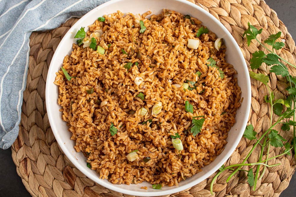 Easy Baked Mexican Brown Rice in a white bowl on a bamboo mat with cilantro and blue towel.