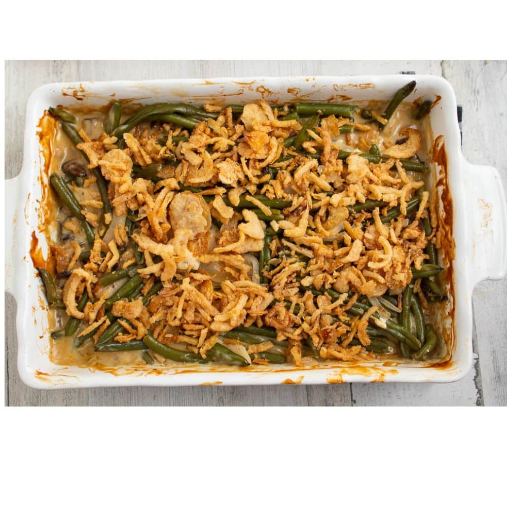 Cooked green bean casserole in a white rectangle casserole dish with unbaked canned french fried onions on top.