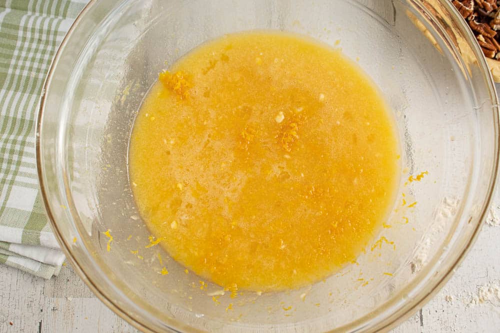 Pie filling with orange zest in a large clear mixing bowl on a grey table.