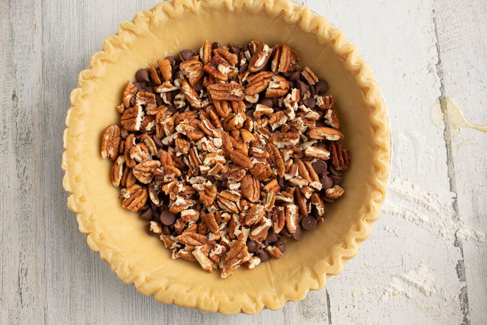 Unbaked pie shell with pecan pieces and chocolate chips.