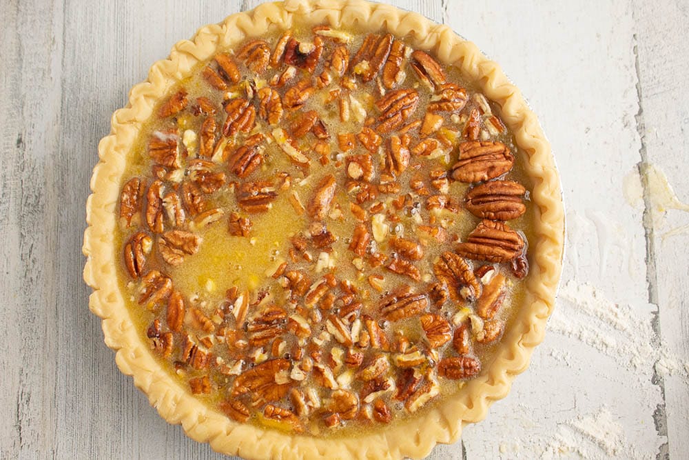 Unbaked Chocolate Orange Pecan Pie. On a grey table with scattered flour.