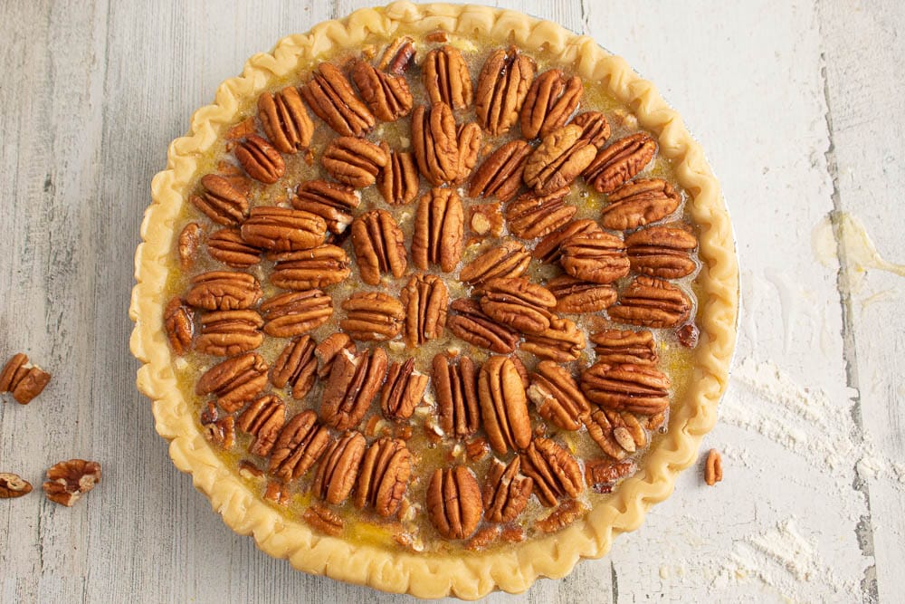 Unbaked Chocolate Orange Pecan Pie with decorative pecans on top. On a grey table with flour and pecan pieces.