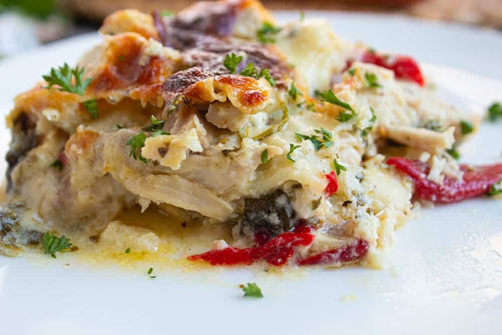 Single serving of white chicken lasagna with spinach and roasted red peppers on a white plate.