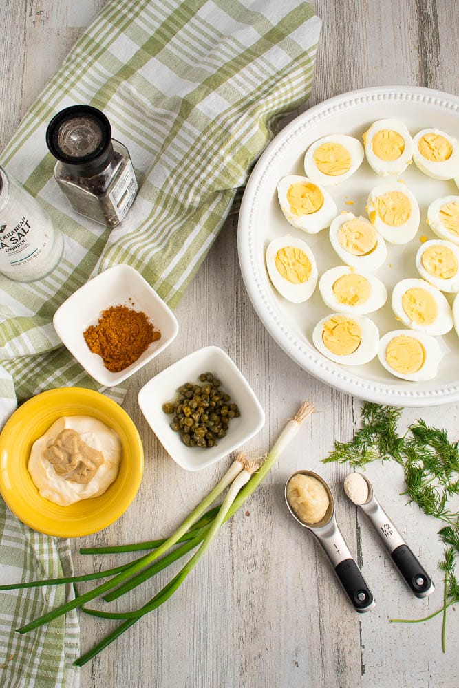 Deviled eggs with curry and dill ingredients on a white wood table with a green and white plaid towel.