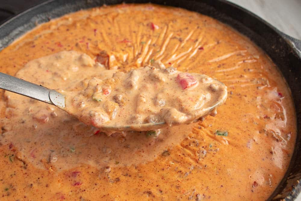 Close up of Spicy Sausage Rotel Queso Cheese Dip in a big silver kitchen spoon.