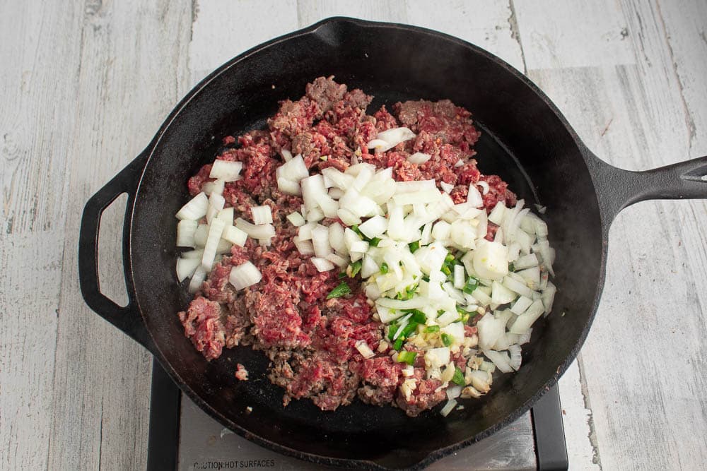 Semi browned sausage, onions, garlic, jalapenos in a cast iron skillet.