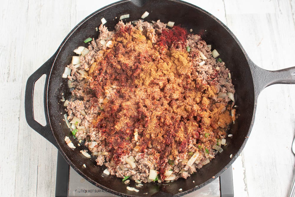 Browned sausage and veggies with seasonings on top in a cast iron skillet.