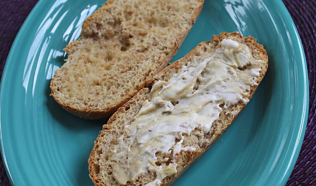 Toasted Hoagie bun sliced in half with mayonnaise and mustard mixture smeared on one half on a blue plate.