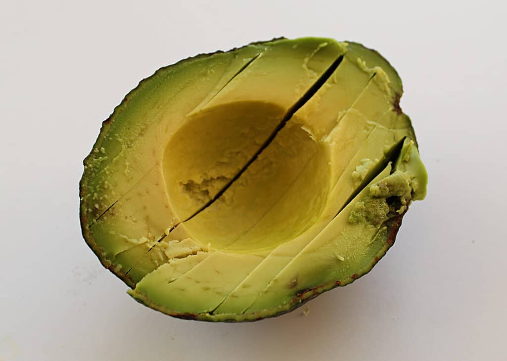 Creamy ripe avocado half scored in slices in the shell.