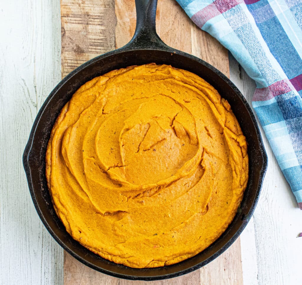 Brown Butter Carrot Soufflé in a cast iron skillet on a wood serving board with a blue plaid towel.