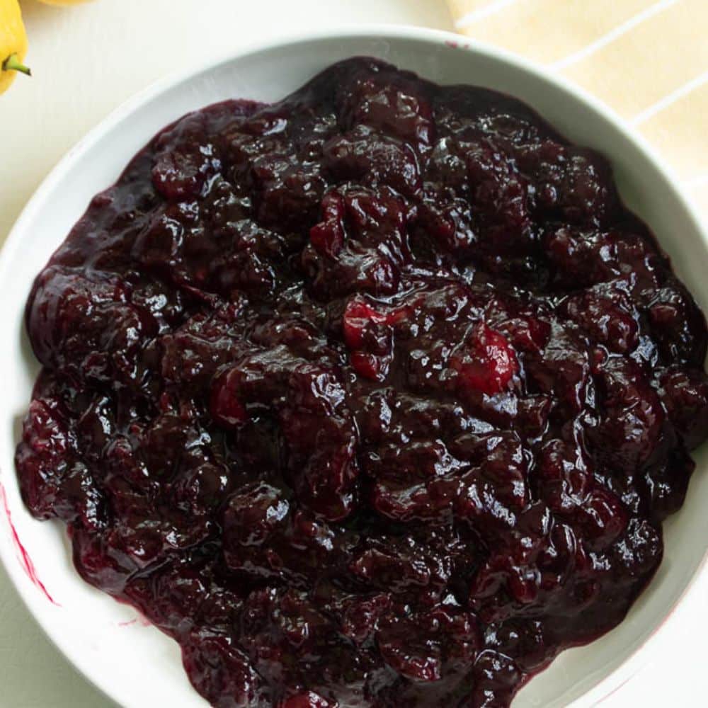 Homemade cherry pie filling in a white bowl on a yellow and white striped towel.