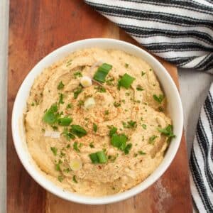 Easy Basic Homemade Hummus in a white bowl on a wood serving board with a black and white towel.