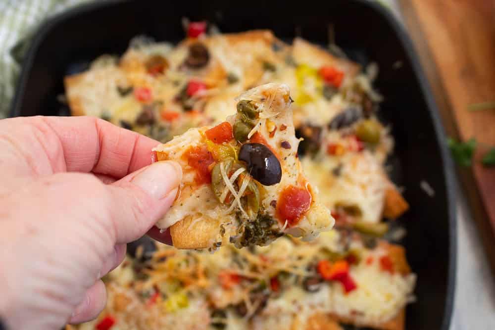 Close up of an Italian nacho over a cast iron skillet full of italian nachos.