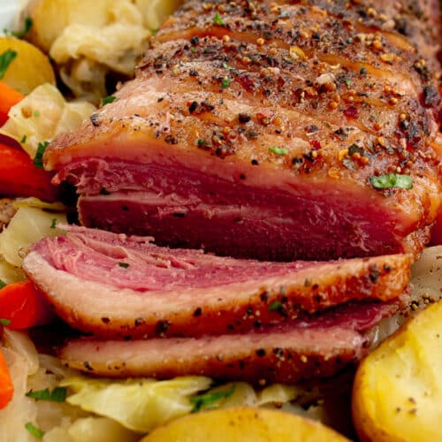 Sliced Dutch oven corned beef and cabbage on a white platter.