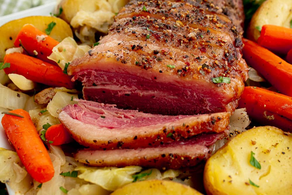 Sliced Dutch oven corned beef and cabbage on a white platter with a green and white towel.