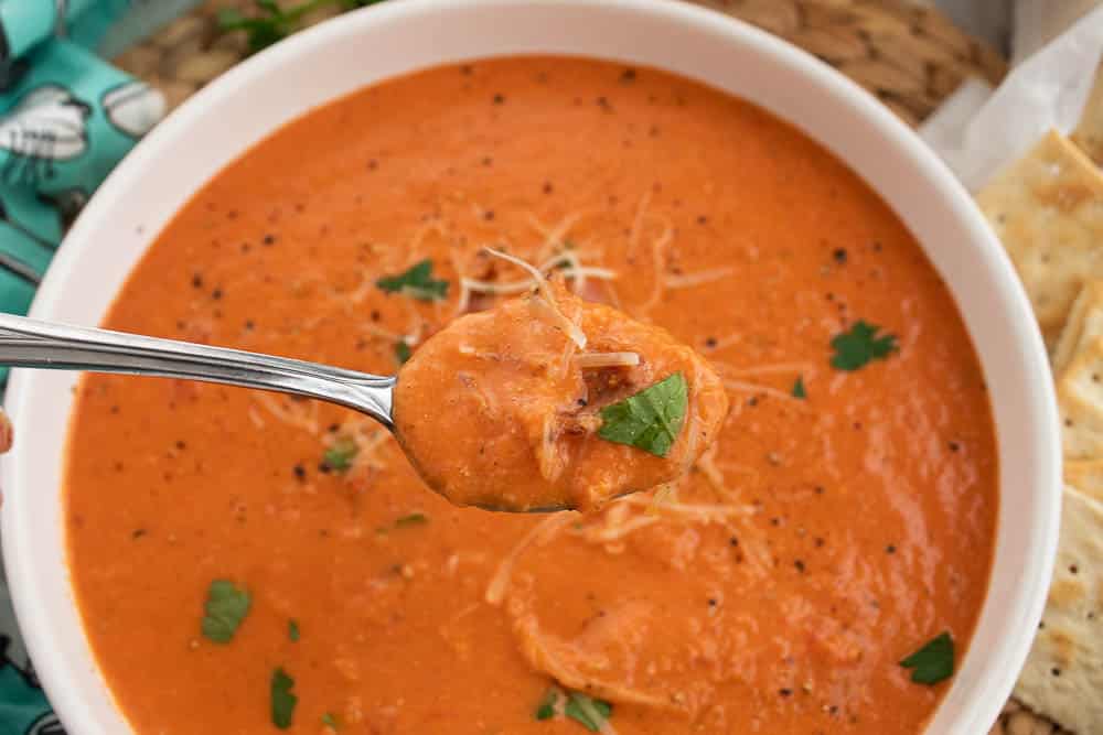 Spoonful of Homemade Bacon Tomato Soup over a  white serving bowl with saltine crackers.