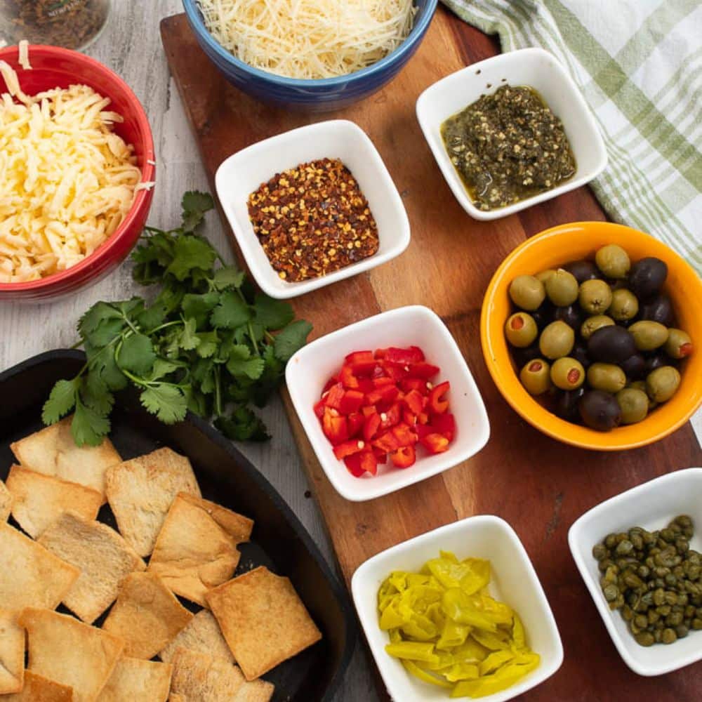 Italian nacho ingredients on a cutting board with a green and white towel.