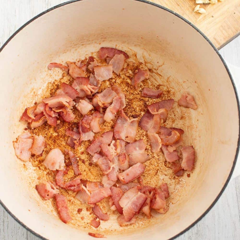 Bacon frying in a white Dutch oven.