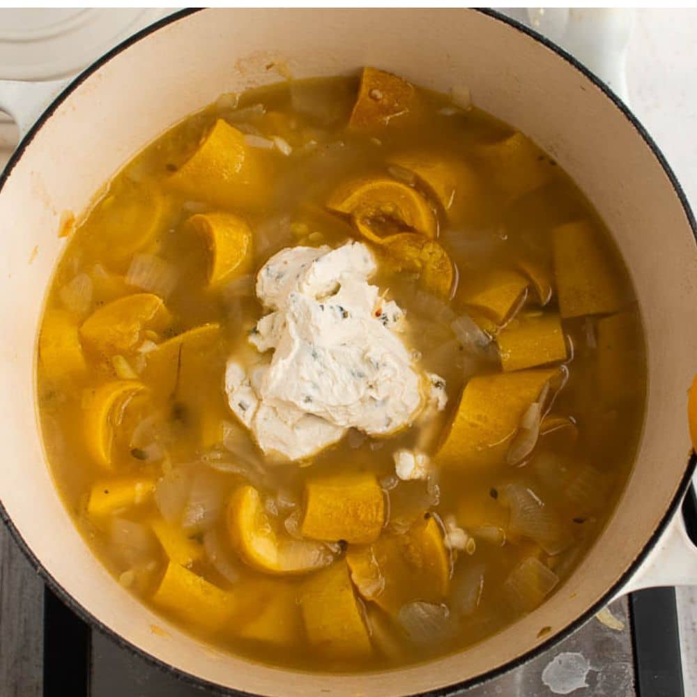 Yellow squash, onions, garlic, thyme, broth, and cream cheese in a white dutch oven.