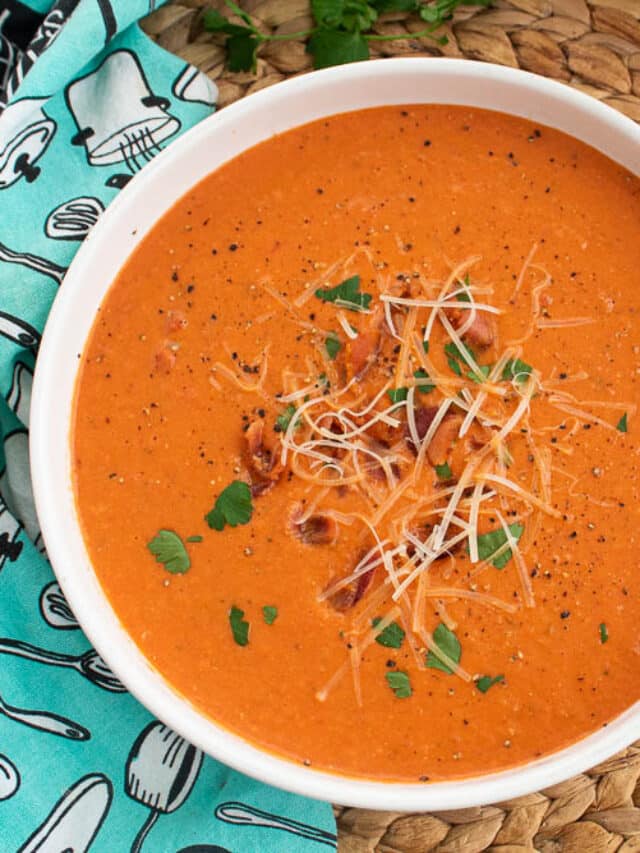 Homemade Bacon Tomato Soup in a white serving bowl on a bamboo placemat, saltines, and blue and white towel.