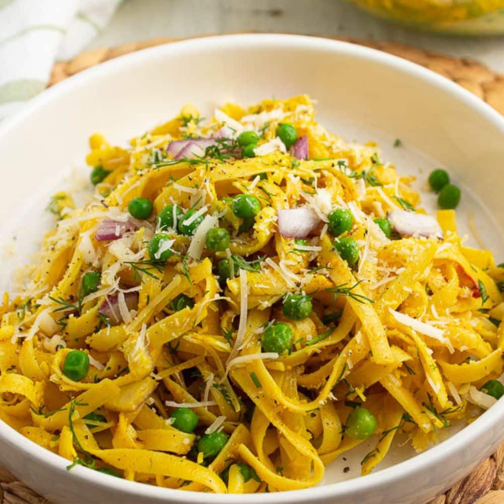 Curry Pasta with fresh dill and peas in a white serving bowl.