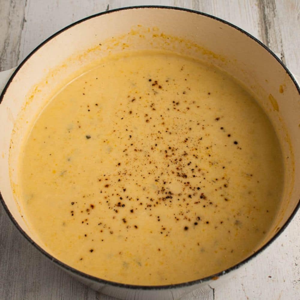 Creamy yellow summer squash soup with parmesan and lemon with fresh ground pepper on top in a white Dutch oven.