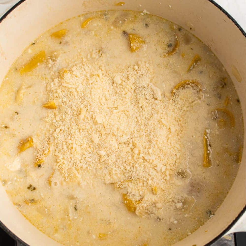 Yellow squash, onions, garlic, thyme, broth, and cream cheese in a white dutch oven with parmesan cheese added.