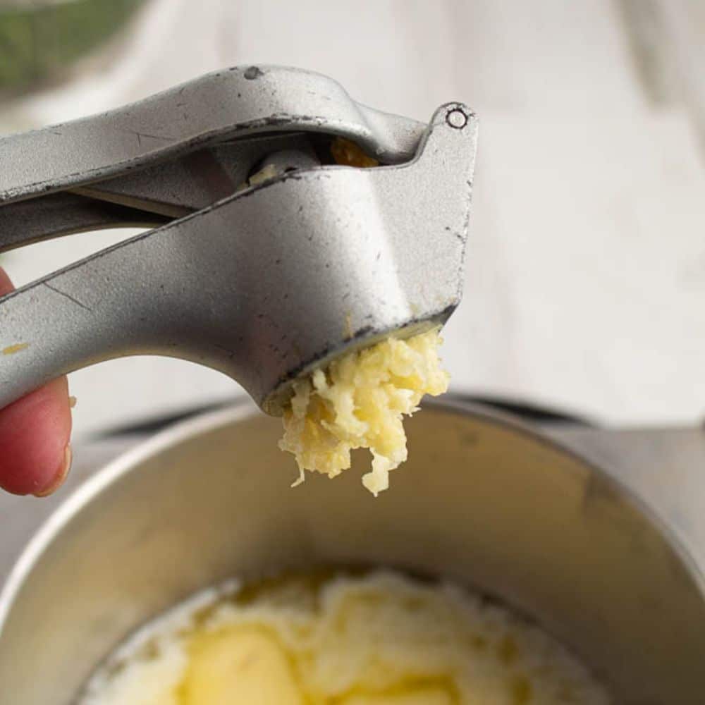 Crushed garlic in a garlic crusher over a saucepan of melted butter.