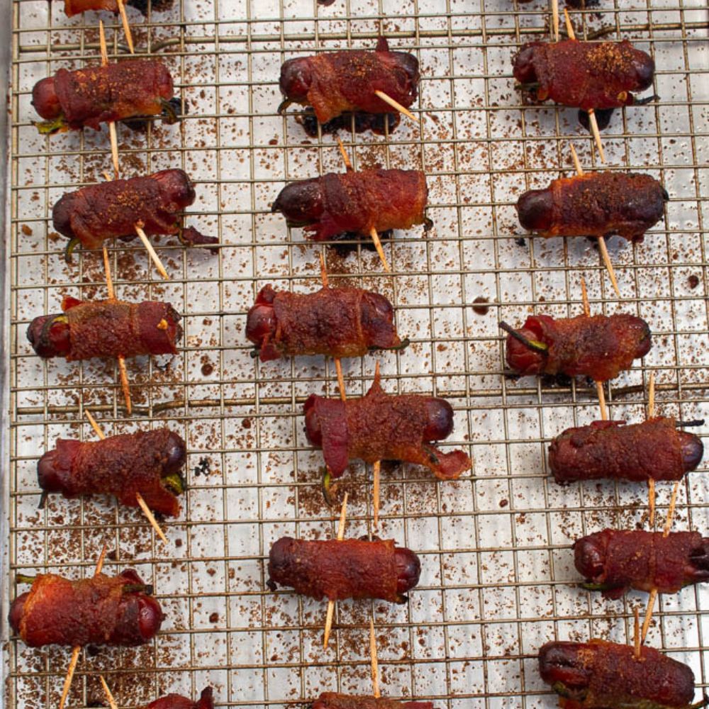 Cooked brown sugar bacon wrapped smokies and jalapenos on a cooking rack inserted on baking sheet.