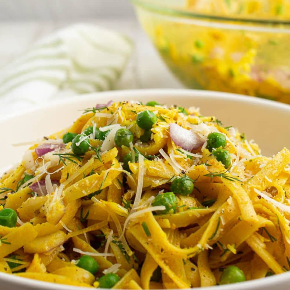 Curry pasta with fresh peas, dill, red onion in a white serving bowl.