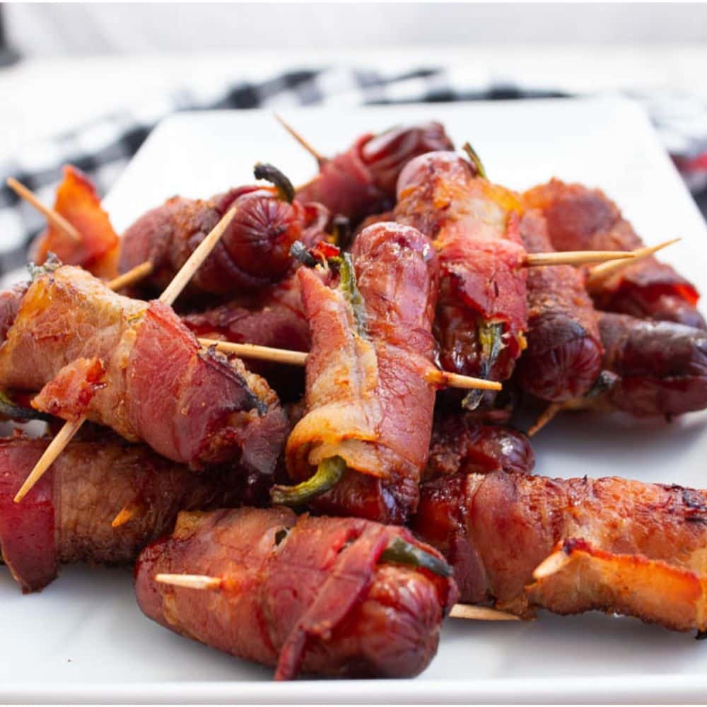 Brown sugar bacon wrapped smokies with jalapeno with toothpicks on a white rectangle serving plate.