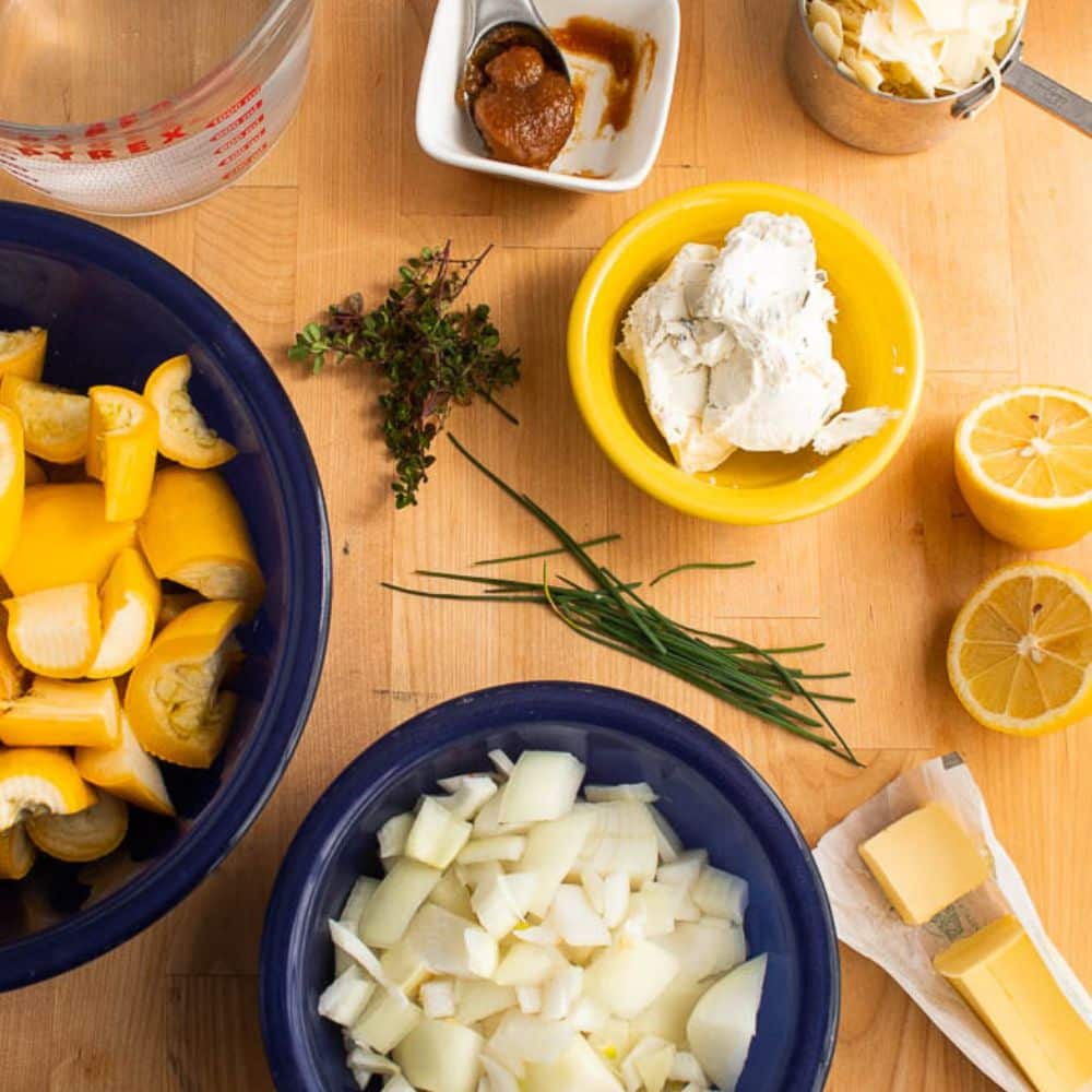 Creamy Yellow summer squash soup with parmesan ingredients on a butcher block cutting board.