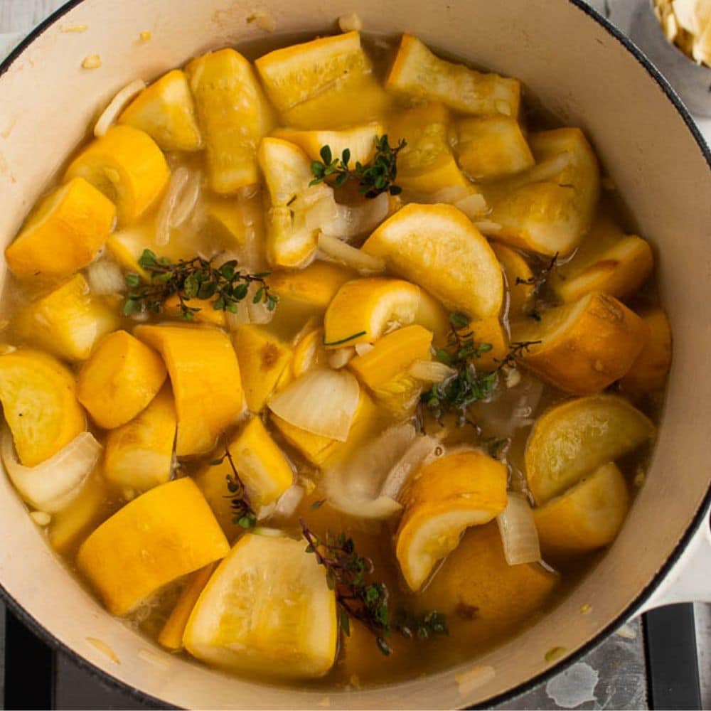 Yellow squash, onions, garlic, thyme and broth in a white dutch oven.